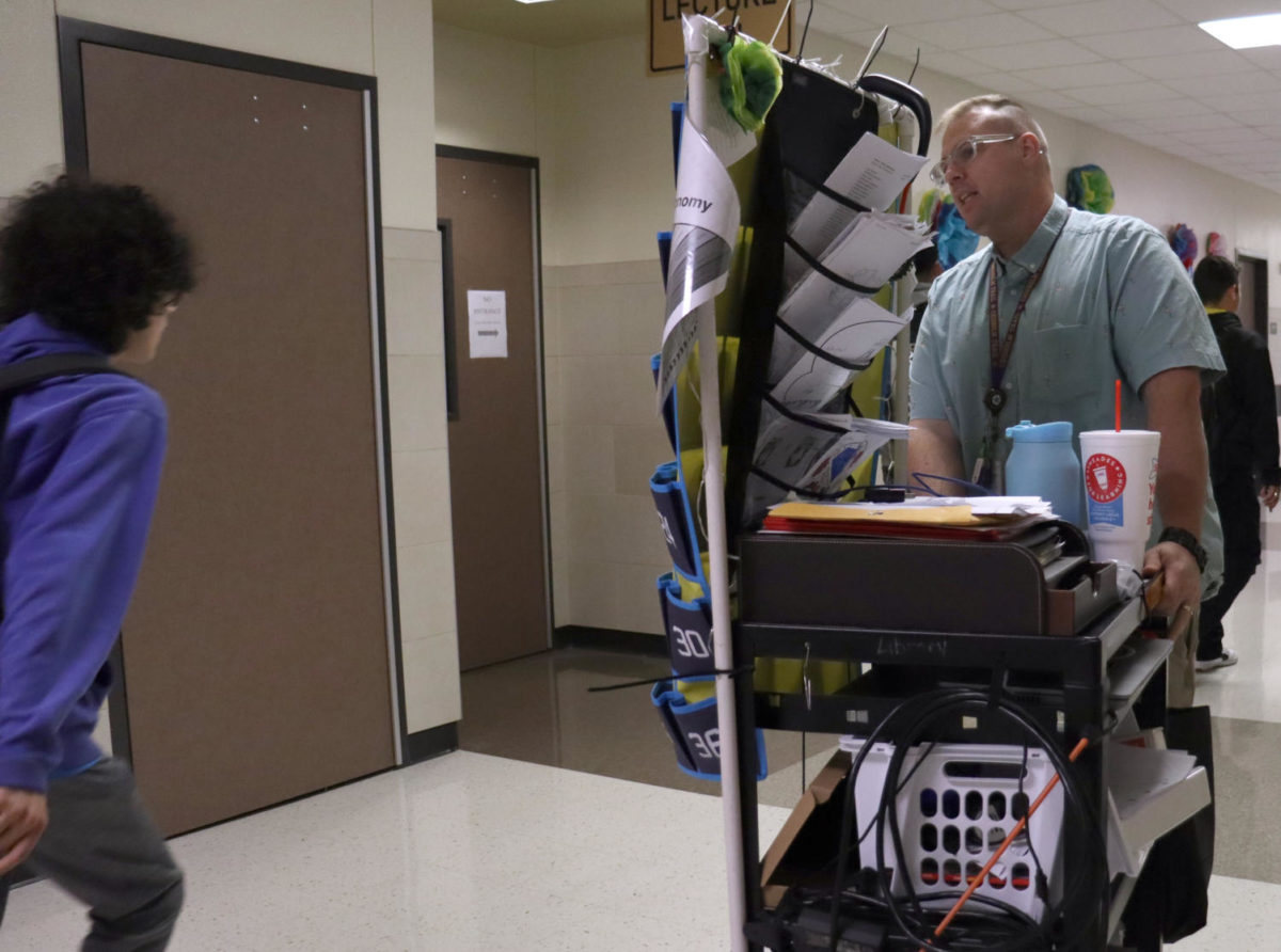 As he heads to his fifth period classroom, Spanish teacher Johnathan Hicks moves his cart down the 300 hallway during the passing period since he does not have a classroom to himself. Photo by Daylin Mitchell-Cochran, 12