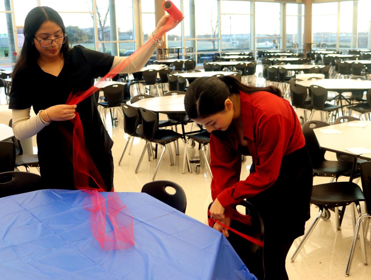 Seniors Sofia Mandonold and Naomi Montez set up their table, tying ribbons around chairs.