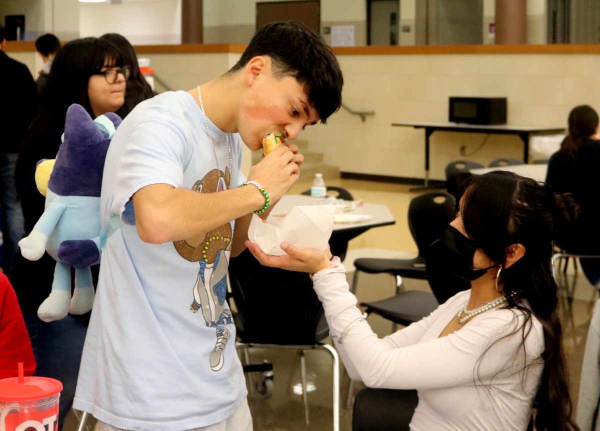 Junior Xavier Mendez eats a banh mi while junior Nivek Solis holds its wrapping underneath. 